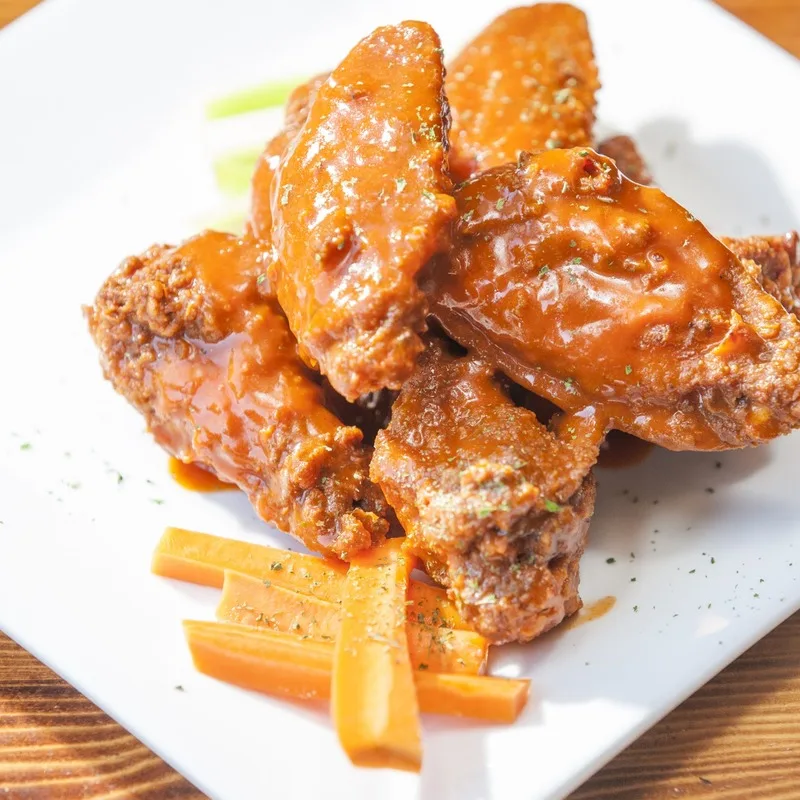 Saucy chicken wings with carrot sticks on a white plate